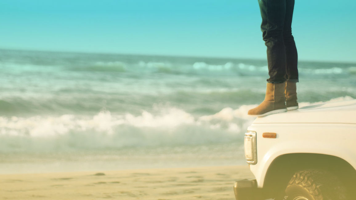 person standing on hood of a 4x4 at the beach